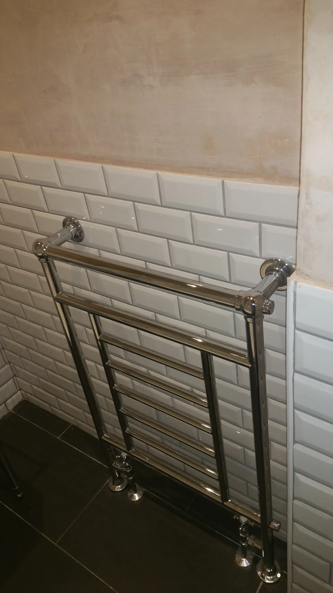 Chrome towel radiator installed in a tiled bathroom